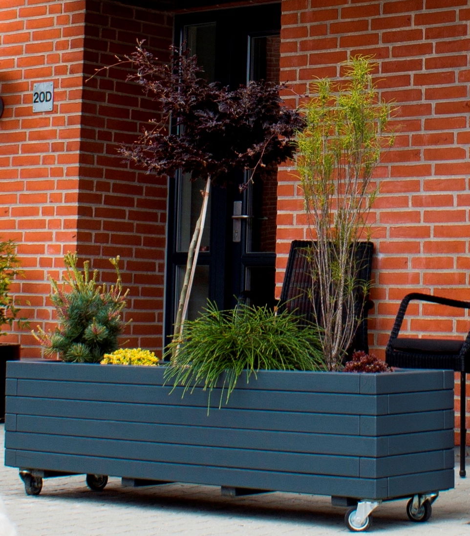 Rektangulær plantekasse på hjul med buske og græs