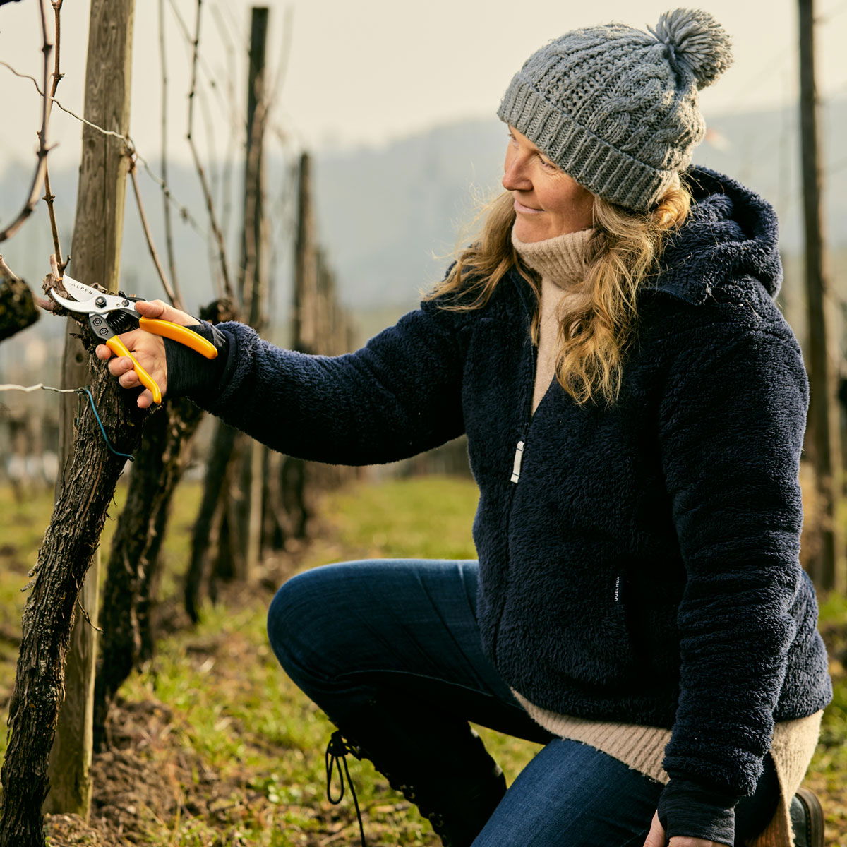 Kvinde i varm jakke beskærer vinranker med saks