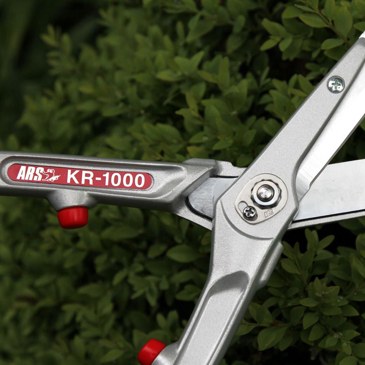 Sølvfarvet ARS KR-1000 hækkesaks foran hæk