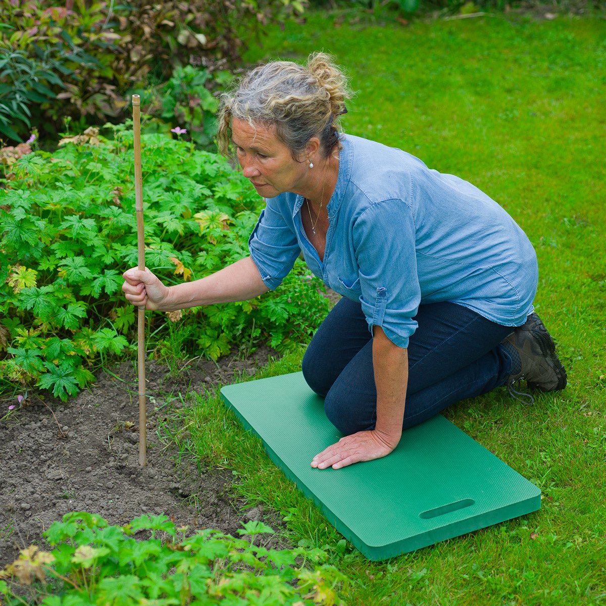 Kvinde knæler i haven på en grøn haveknaepude