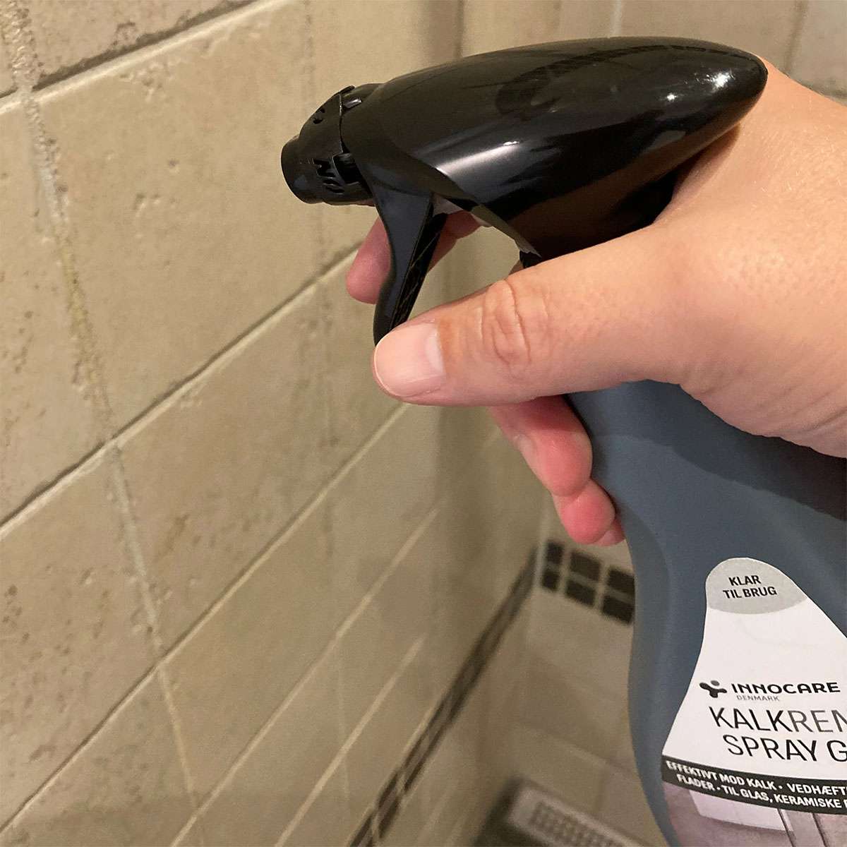 Hånd bruger kalkfjerner spray på badeværelsesfliser