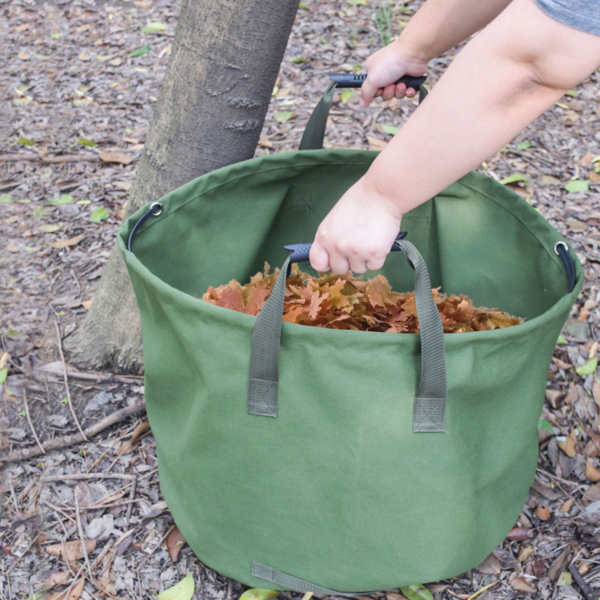 Person samler visne blade i stor grøn havetaske