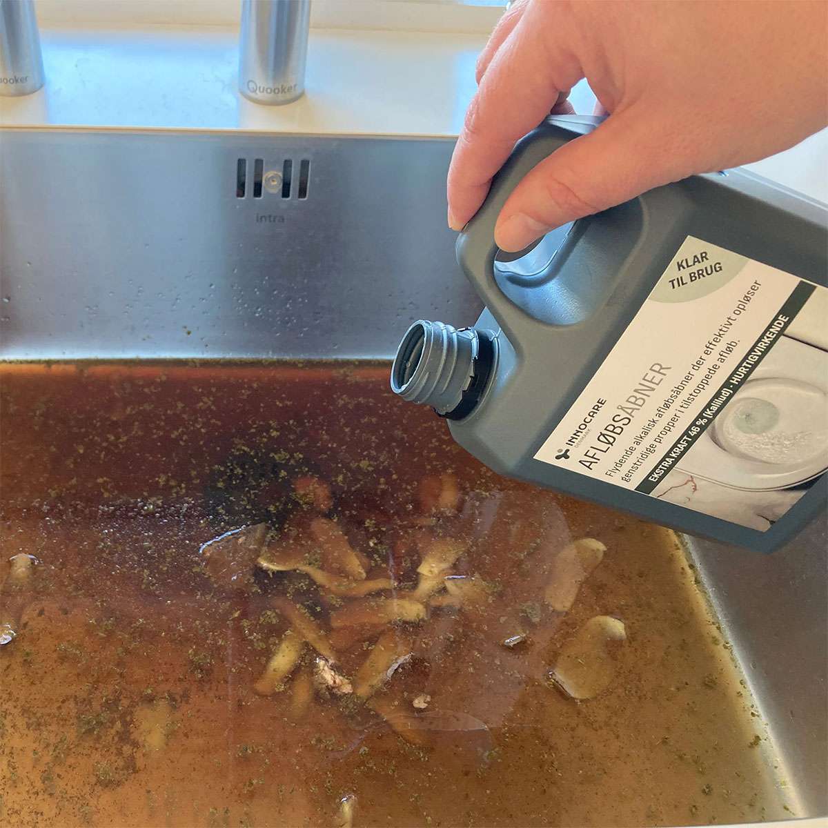 Hånd hælder flydende afløbsrens i tilstoppet køkkenvask