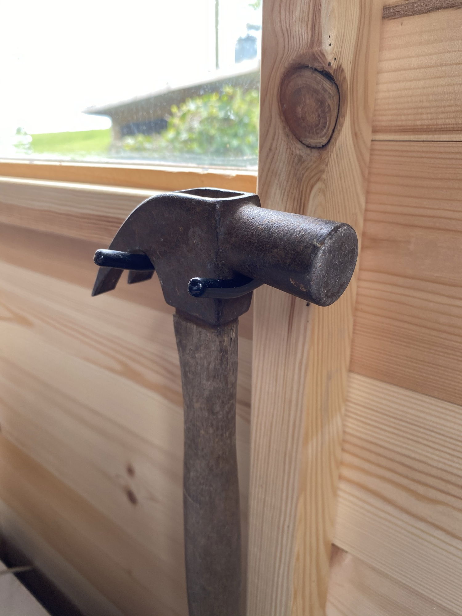 Klodset hammer med træskaft lænet mod trævæg