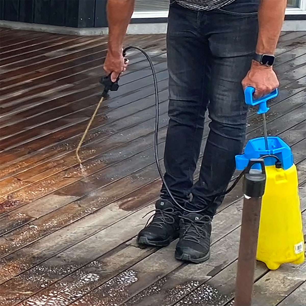 Person rengør træterrasse med gul tryksprøjte