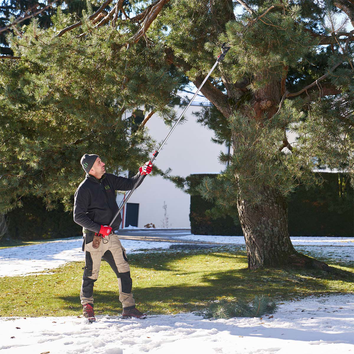 Havearbejder beskærer grene med teleskopsaks i sneen