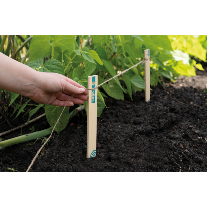 Hånd spænder snor mellem træpinde i køkkenhave