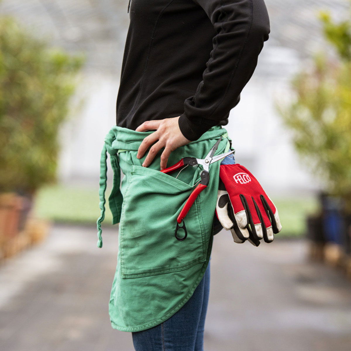 Person med grønt haveforklæde, handsker og beskæresaks