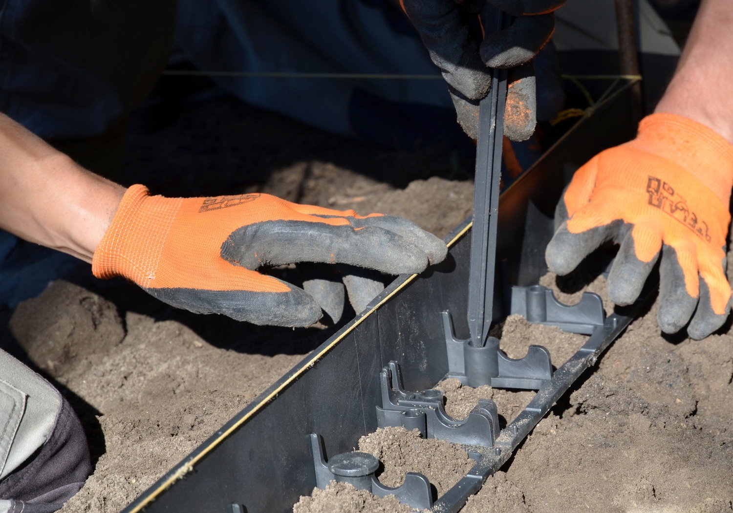 Hænder i arbejdshandsker monterer plastkant i jord