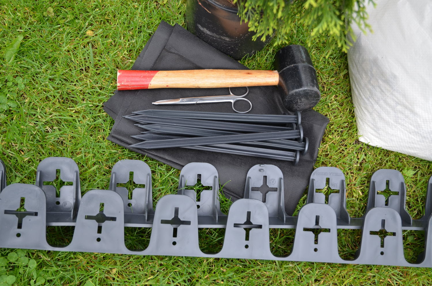 Havekant i plast med pløkker og værktøj på græs