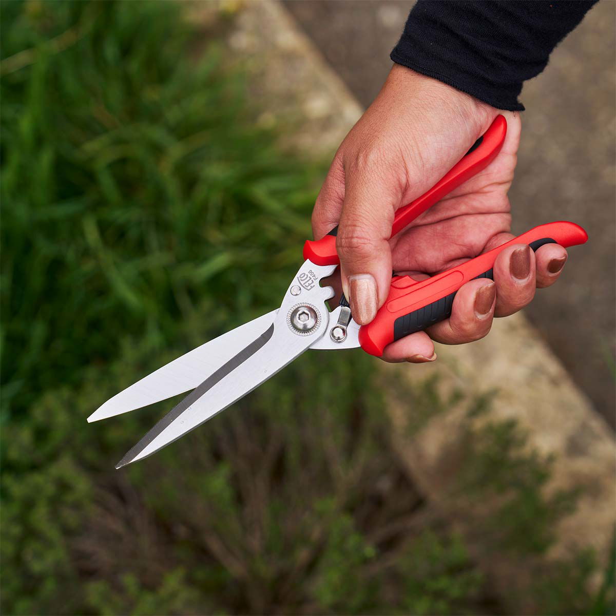 Haveplænesaks med rødt håndtag holdt i hånden