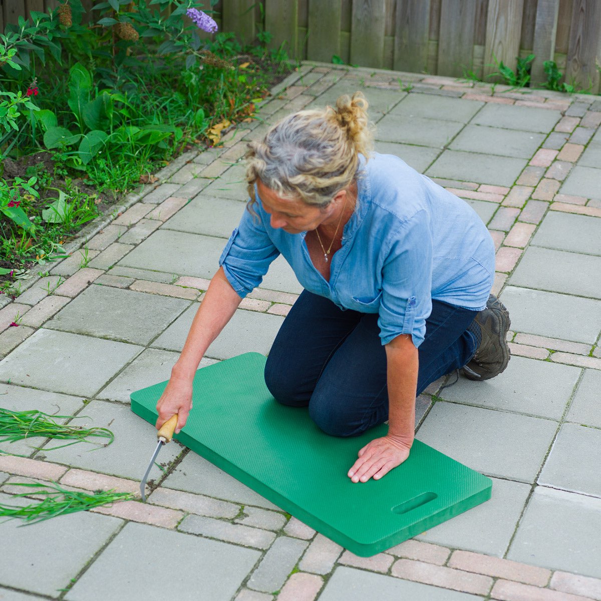 Person bruger grøn knæpude til ukrudtsfjernelse