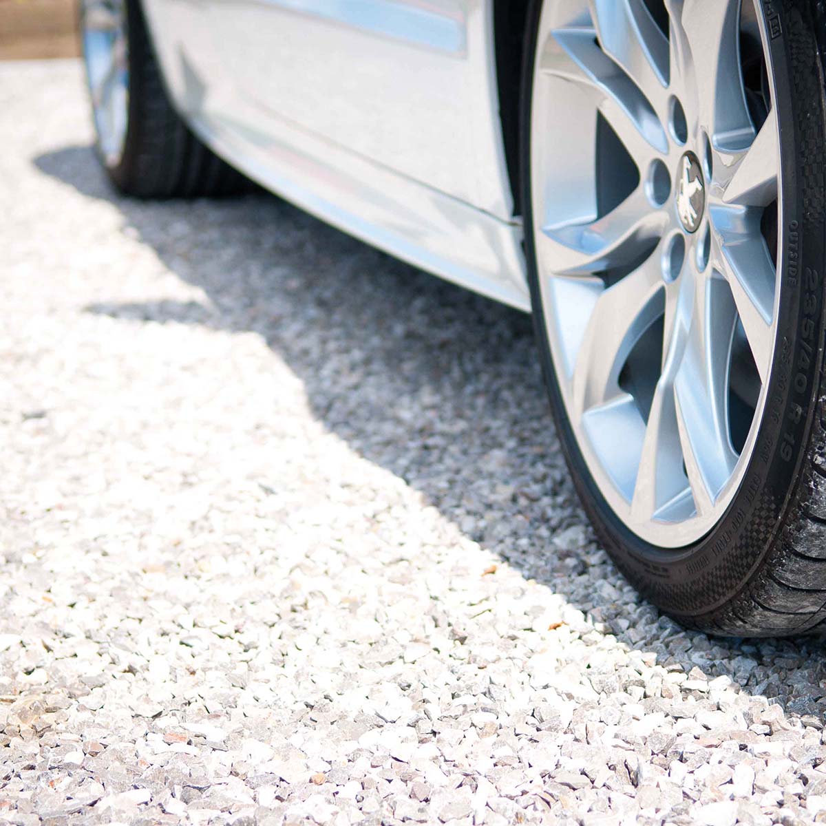 Bilparkeret på indkørsel med lyse granitskærver