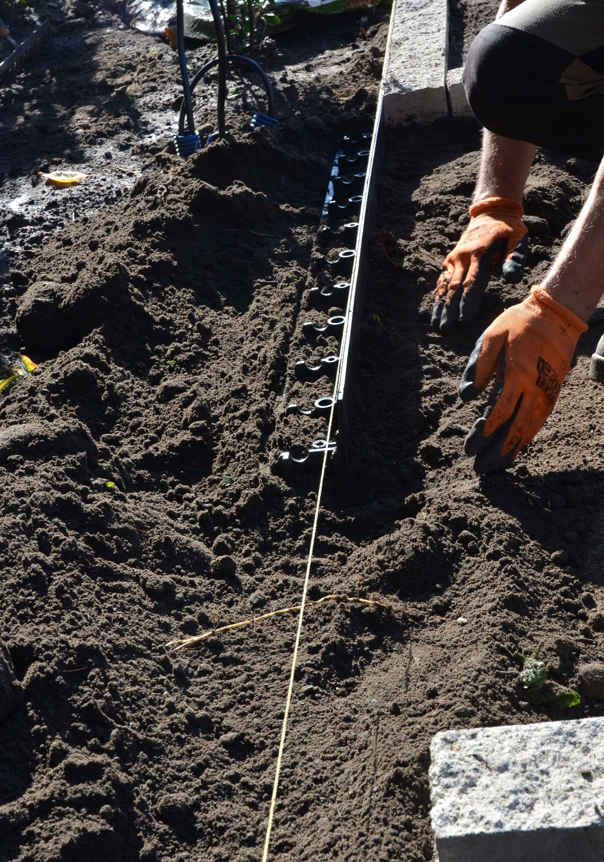 Person monterer plastkant i jord med handsker på