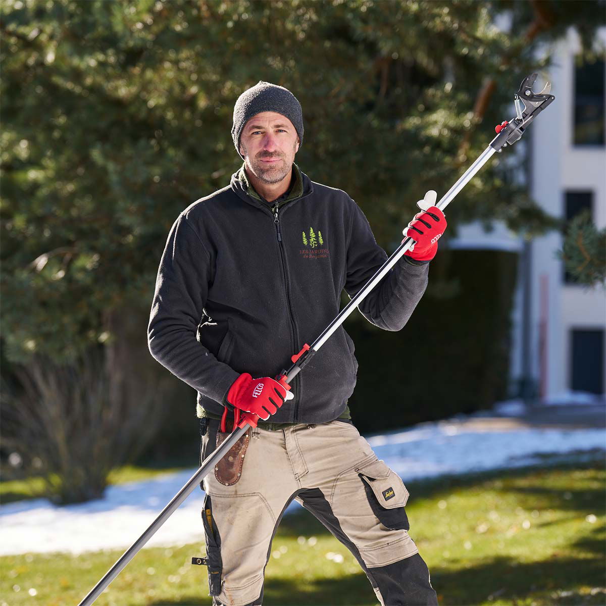 Mand beskærer træ med teleskopgrensaks i haven