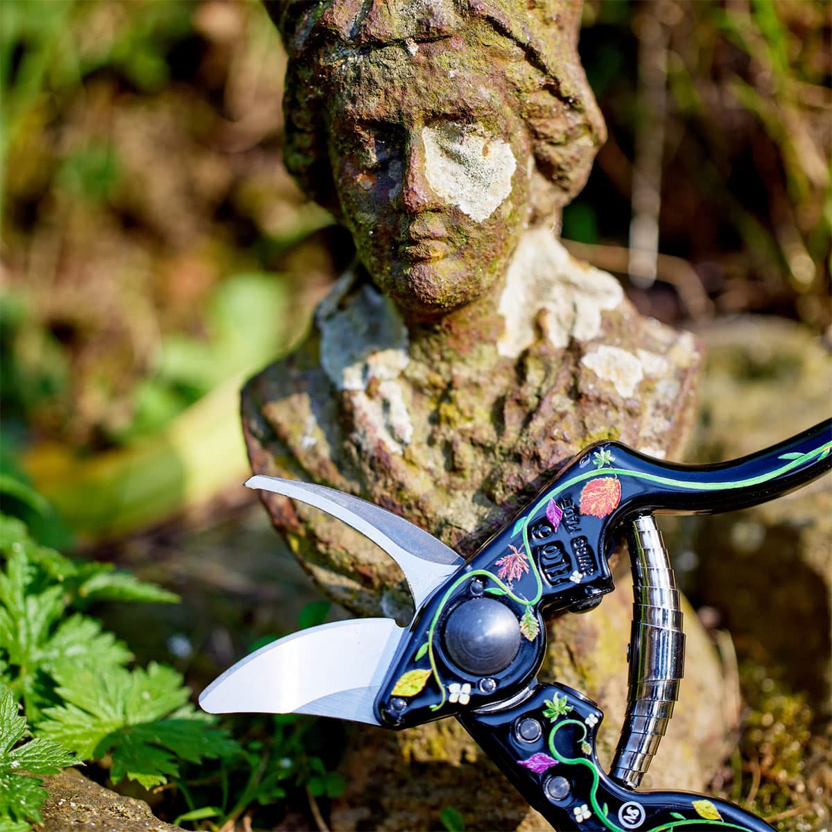 Dekorativ beskæresaks med blomster ved havefigur