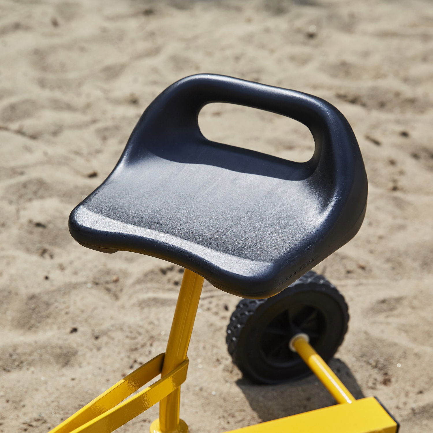 Sort sæde på gult børnekøretøj i sandet